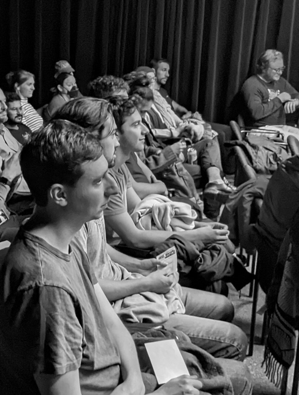 A group of people are sitting in chairs in front of a black curtain.