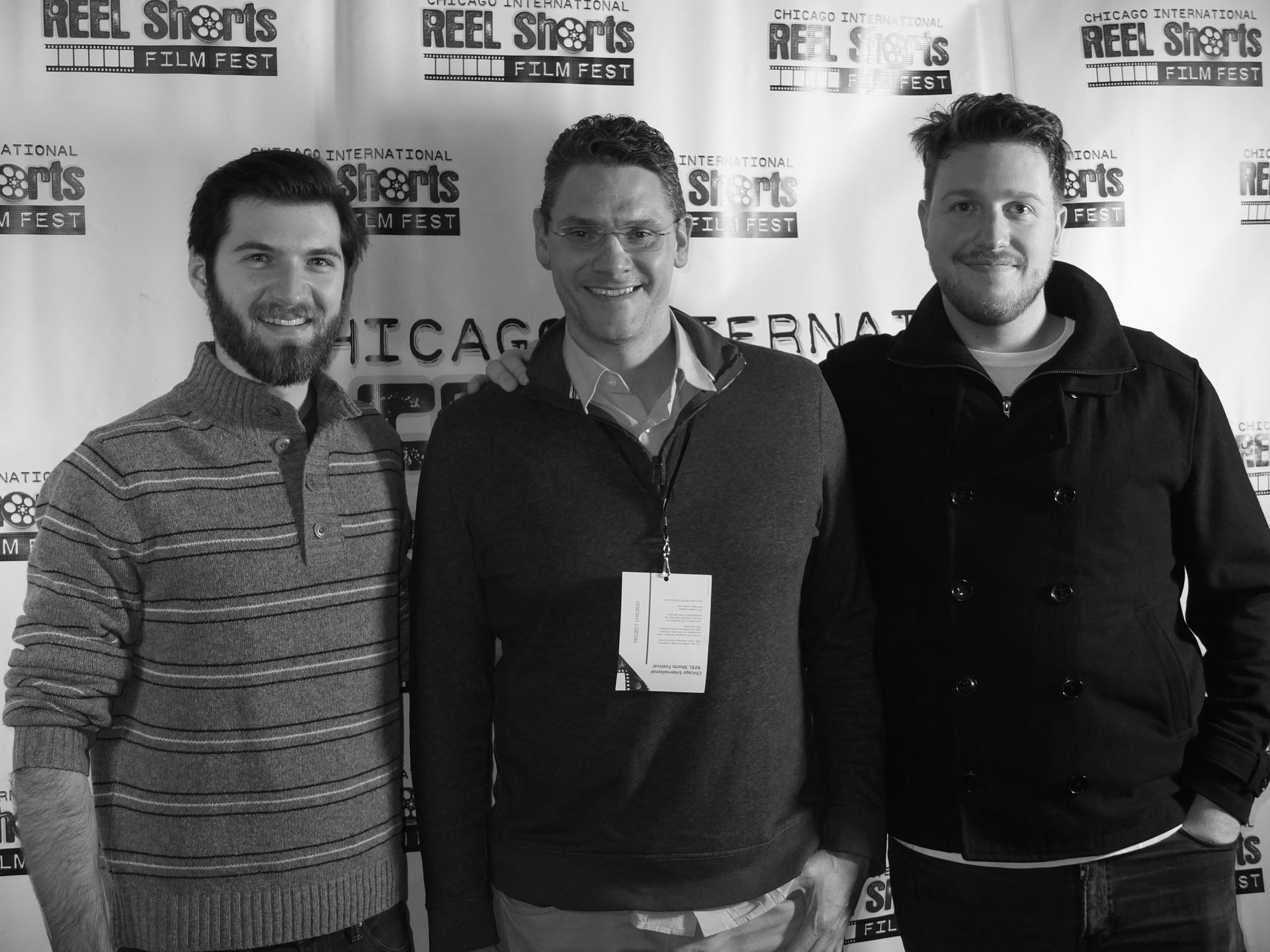 Three men smiling at a film festival, posing in front of a backdrop. Black and white photo.