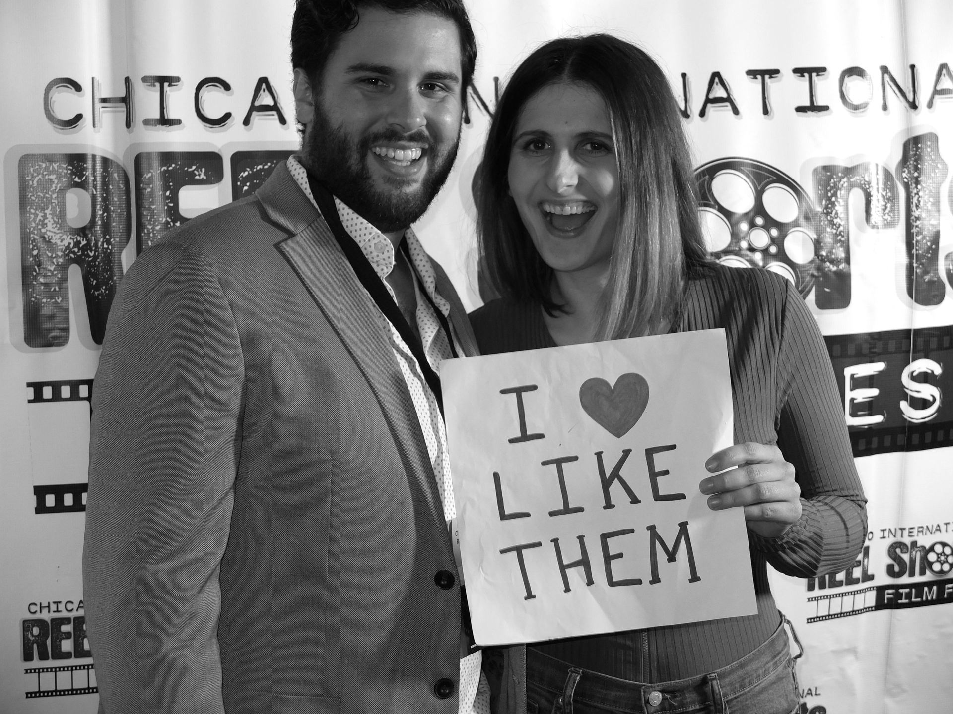 Man and woman smiling, holding a sign that reads 