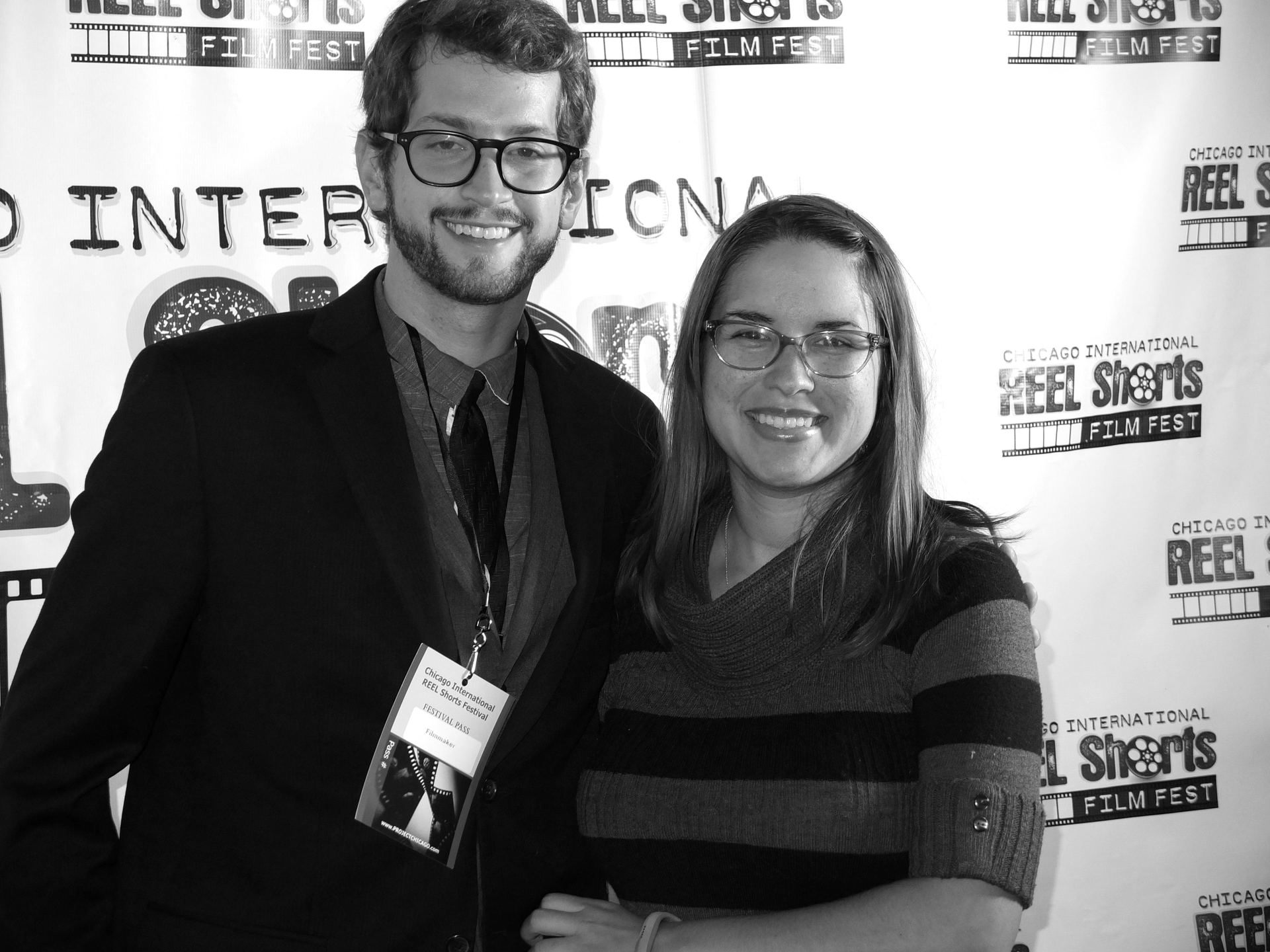 Man and woman in glasses smile at a film festival. They are at a black and white event.