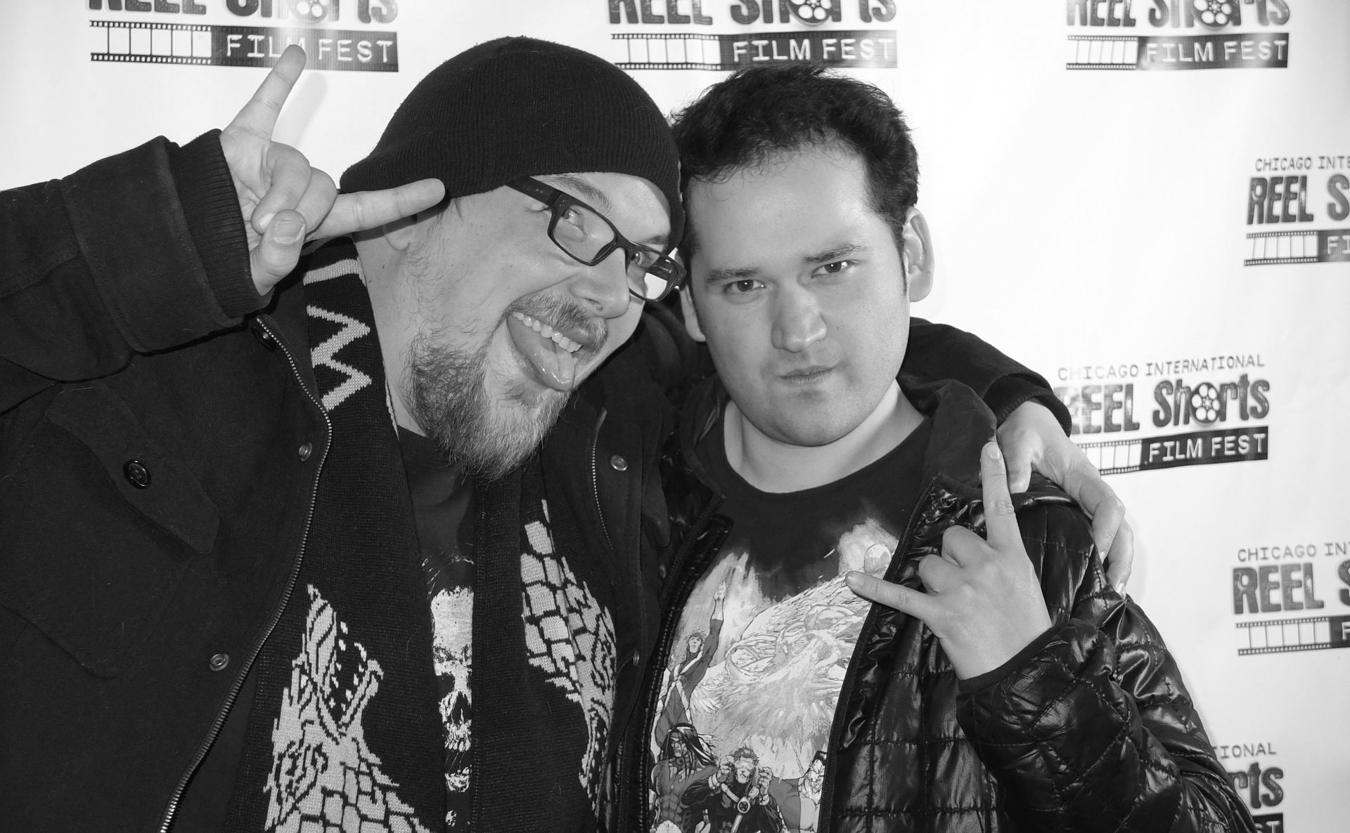 Two men posing for a photo at a film festival. One makes a peace sign, the other a rock-on hand gesture.
