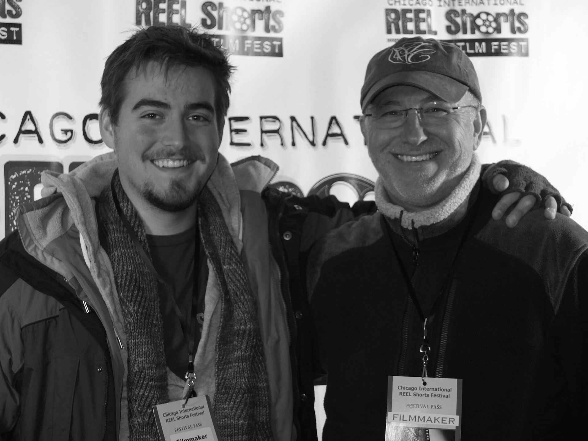 Two men smiling at the Chicago International Reel Shorts Film Fest. One has his arm around the other. Black and white.