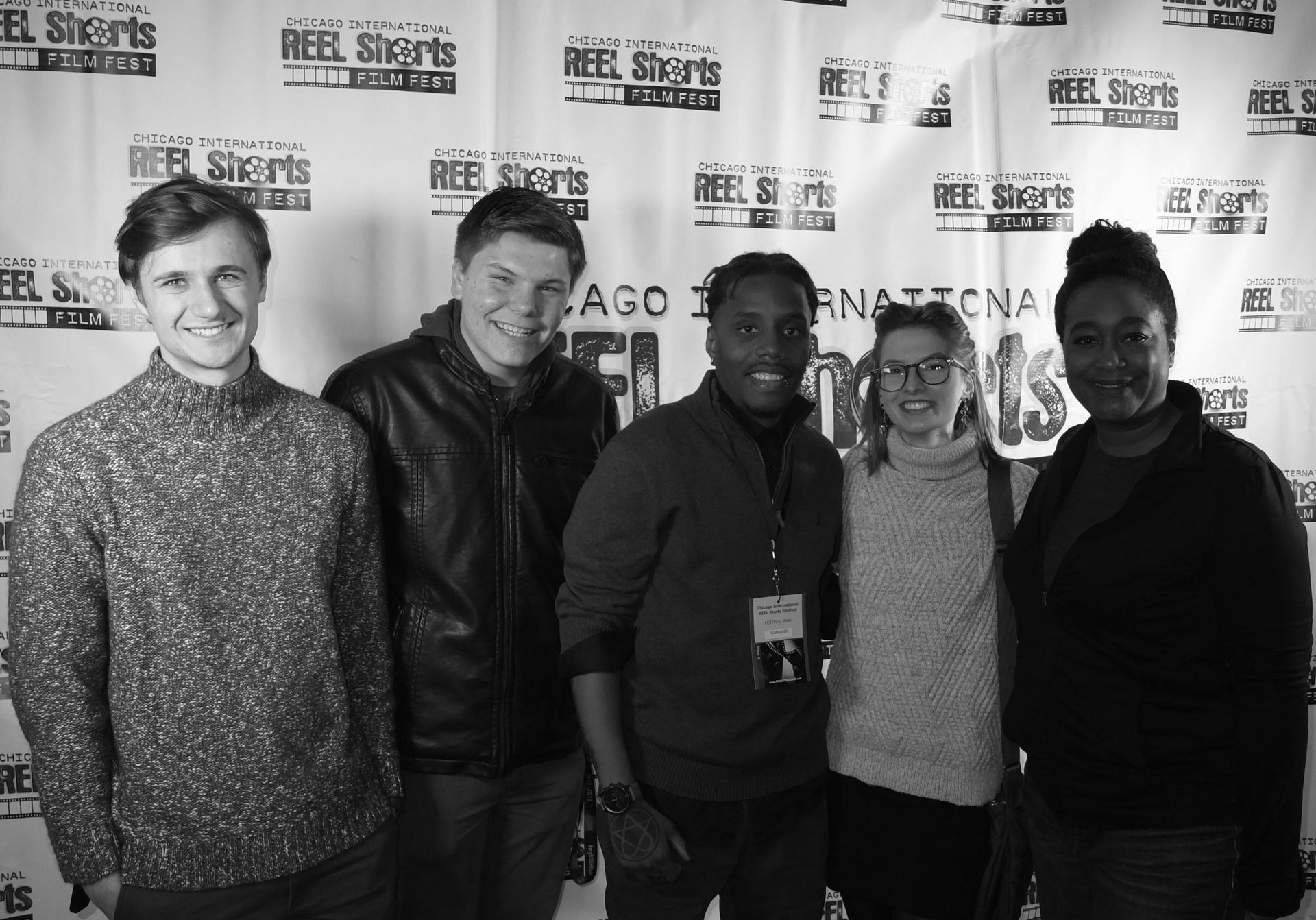 Five people smiling at a film festival backdrop. Two men and three women, black and white photo.