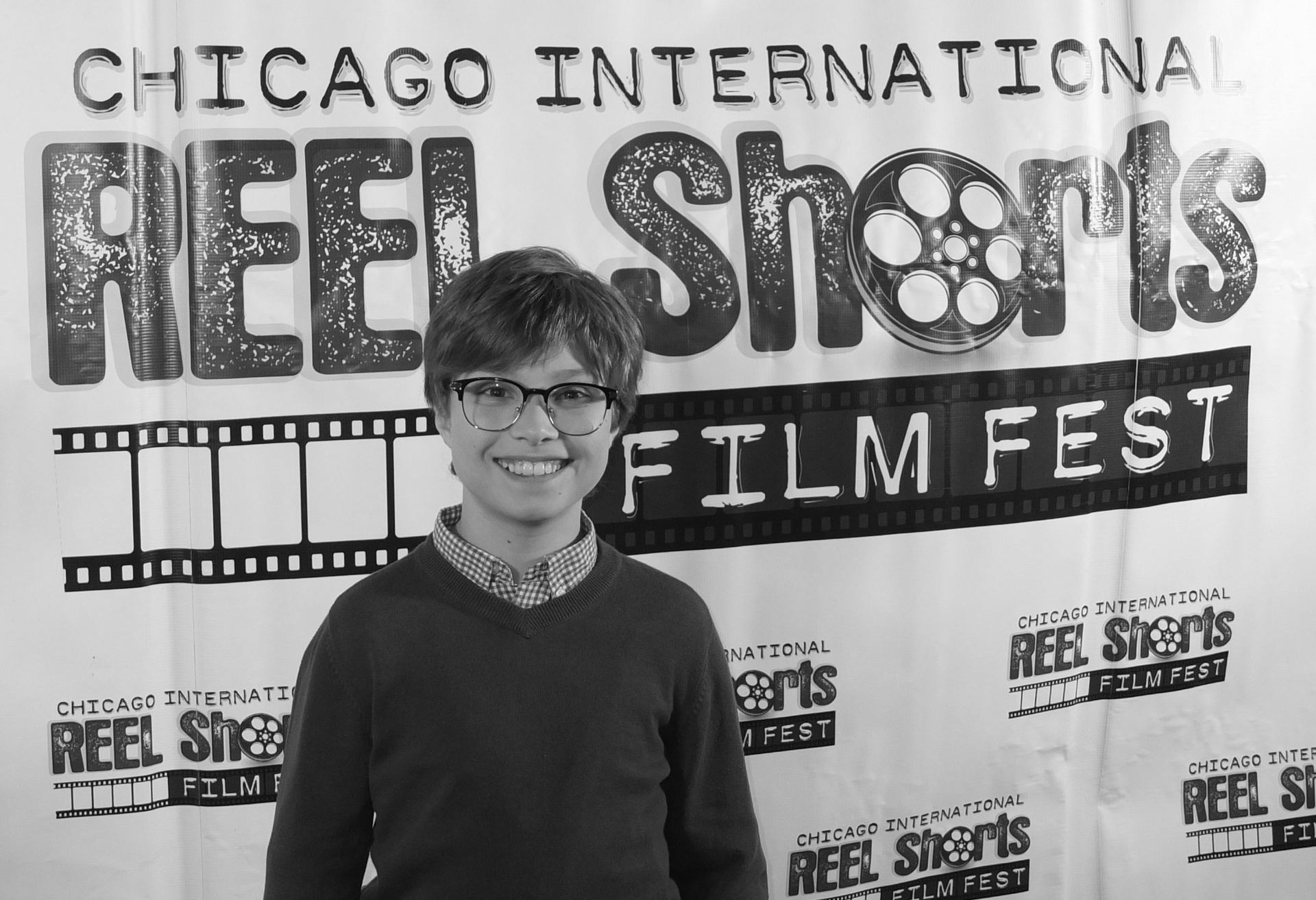A young person smiling in front of a banner for the Chicago International Reel Shorts Film Fest.