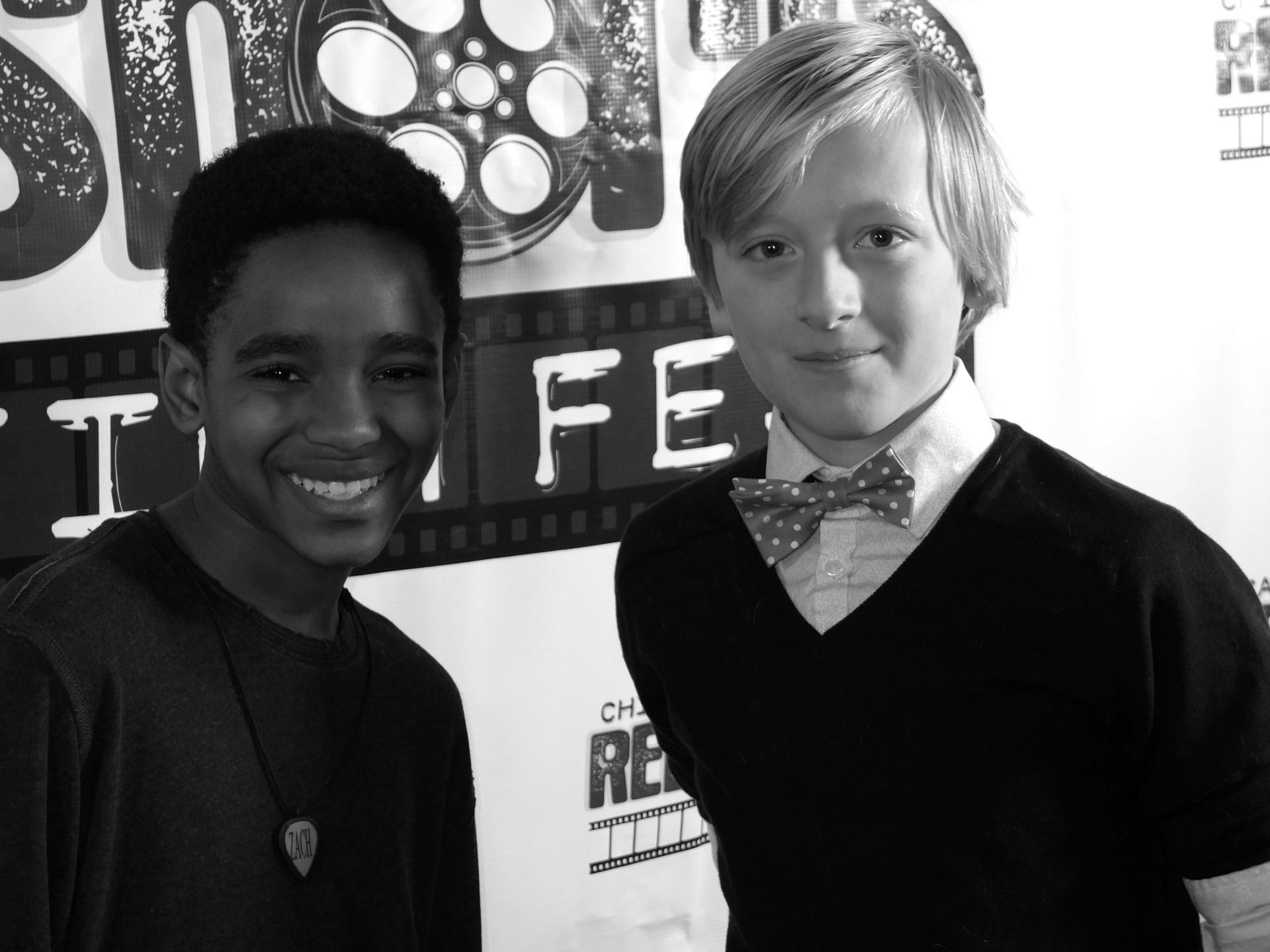 Two boys smiling at the camera, one with a bowtie, at a film festival.