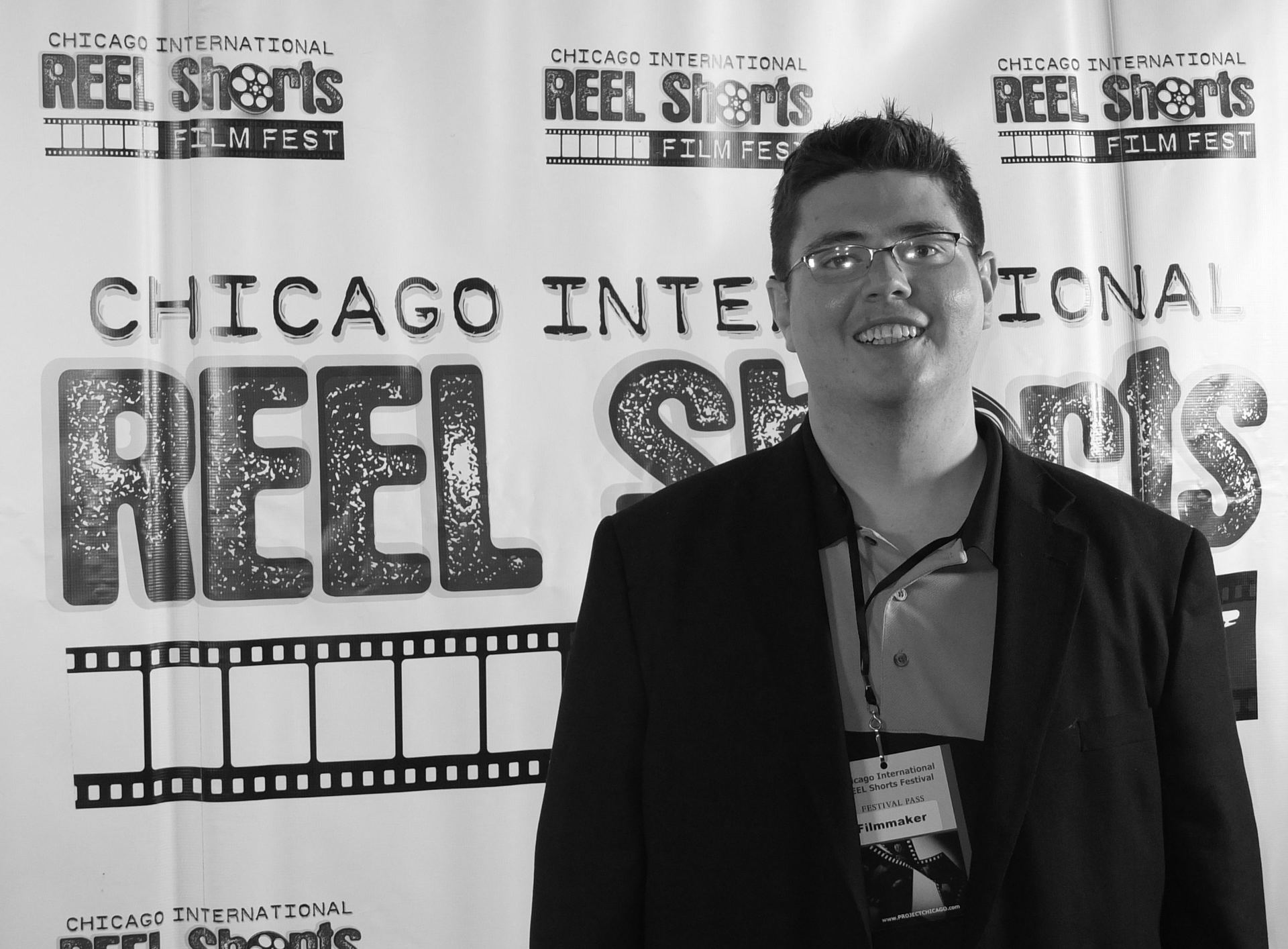 Man at the Chicago International REEL Shorts Film Fest. Smiling, wearing glasses and a black suit.