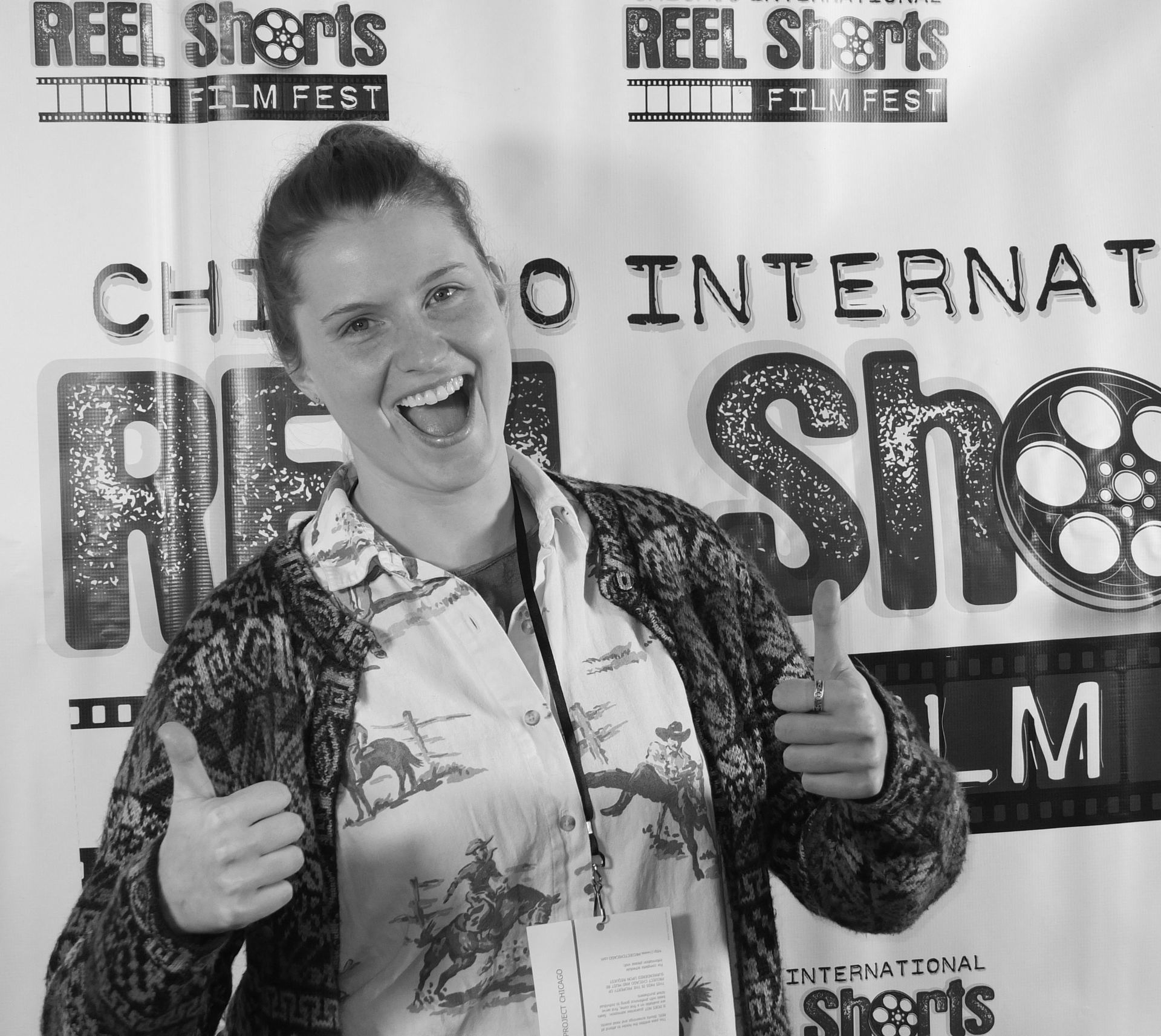 Woman smiles, gives thumbs up at Reel Shorts Film Fest. Black and white photo.