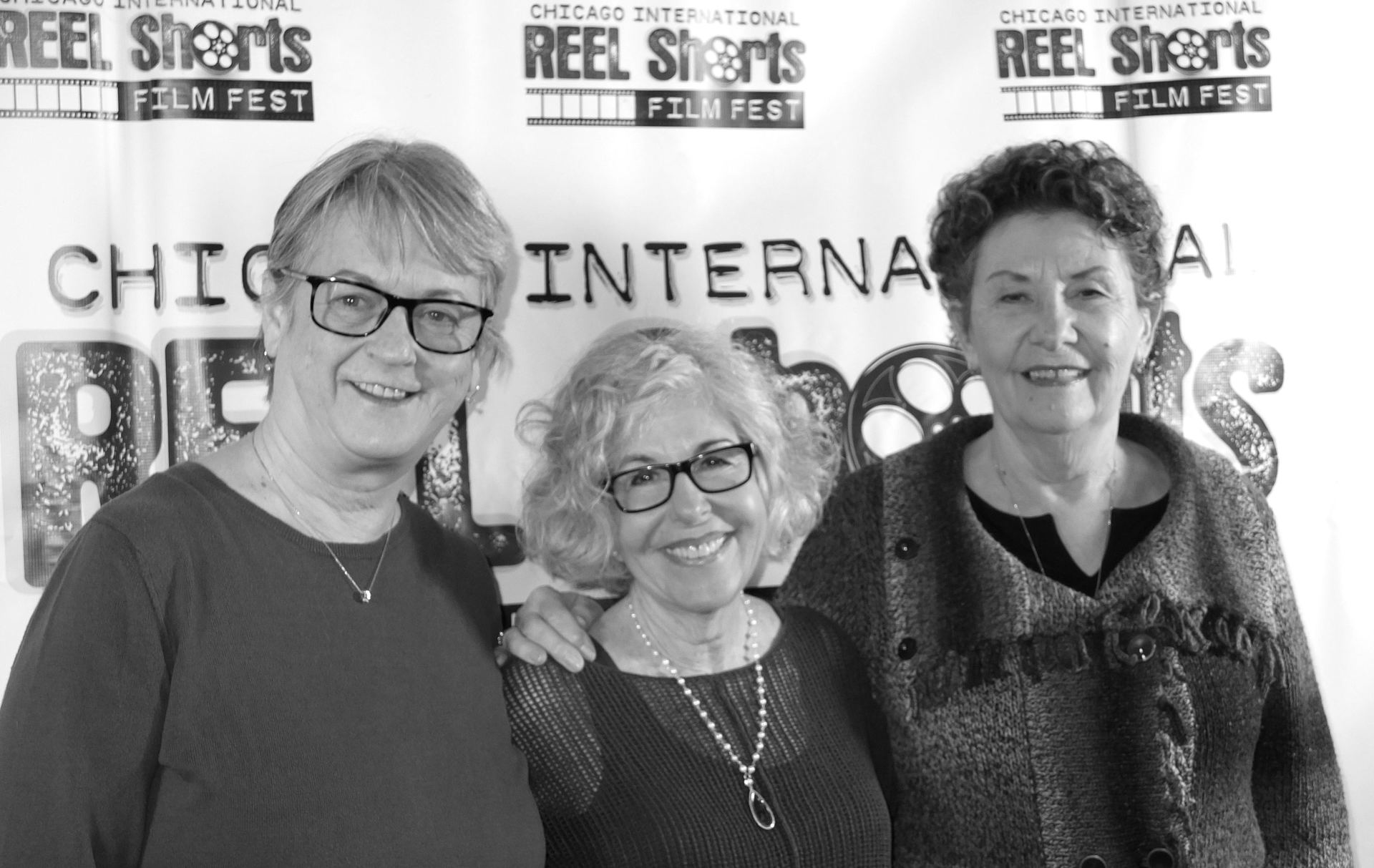 Three women smiling in front of a film festival backdrop.