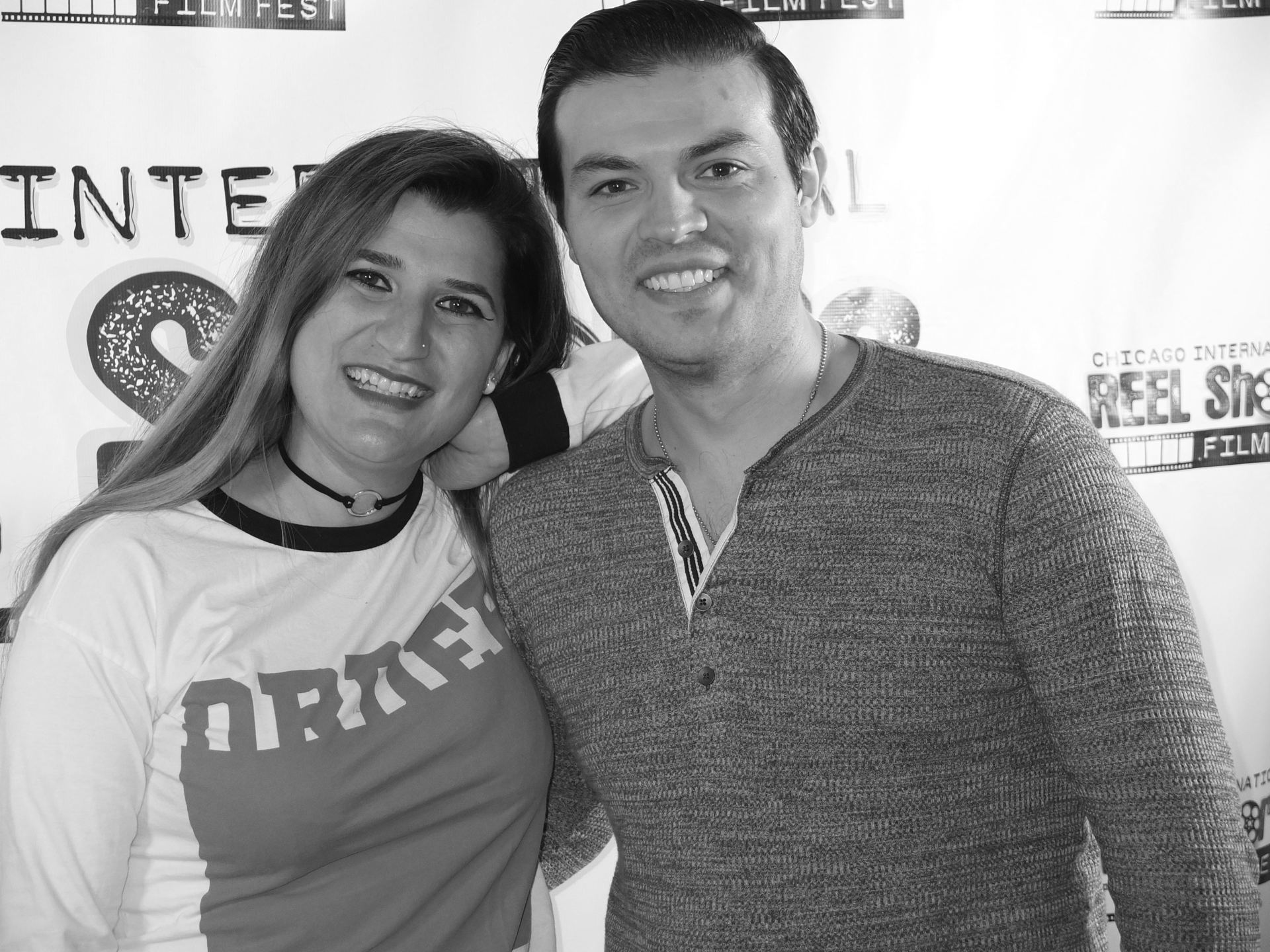 Two smiling people posing for a photo at an event. Woman wears a shirt with 