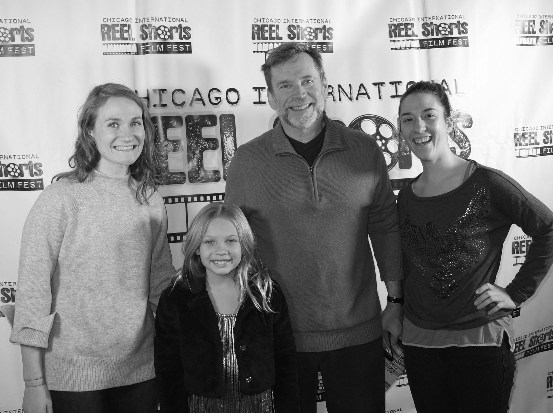 Four people pose at a film festival event. Two women, a man, and a young girl smile in front of a backdrop.