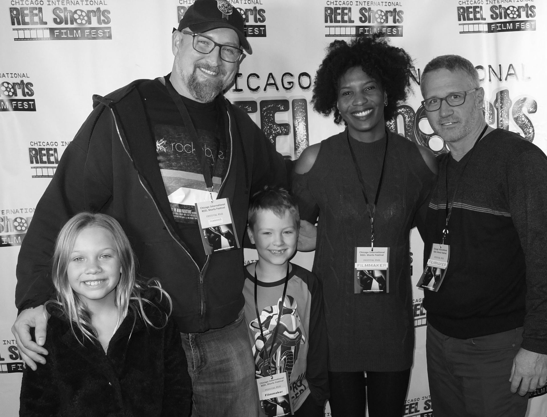 Group of five people smiling at a film festival. Two men, one woman, and two children pose by a backdrop.