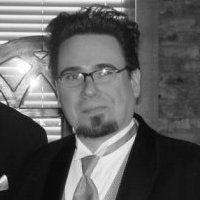 Man in formal wear, glasses, goatee, indoors with blinds and a wall.