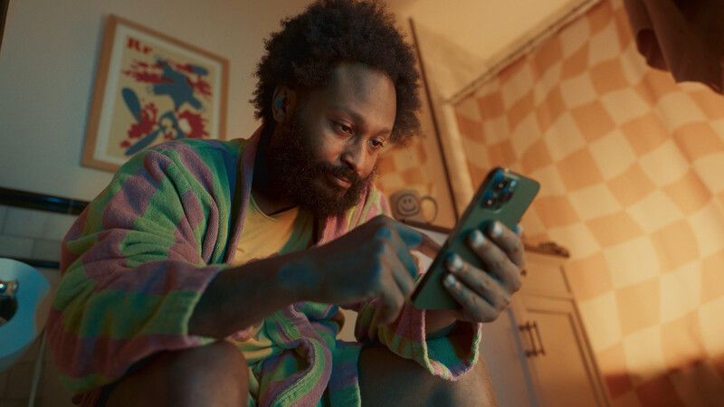 Man in colorful robe using phone in bathroom, warm lighting.