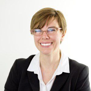 A woman wearing glasses and a black jacket is smiling for the camera.