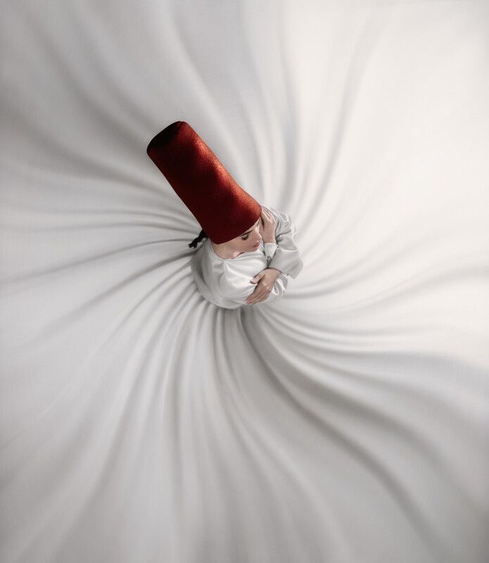 A child in white robes and red fez spins on white fabric.