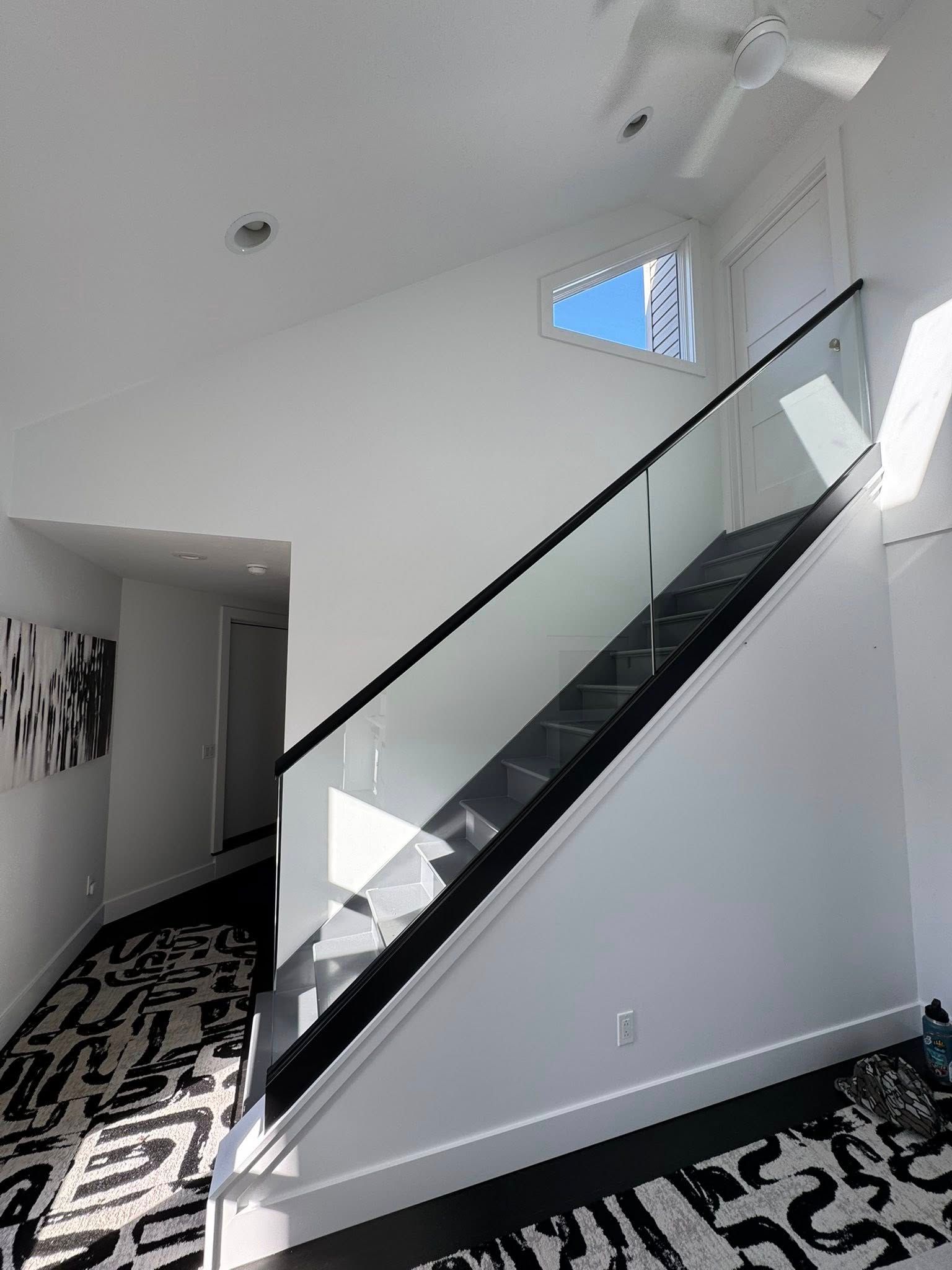 Interior with stairs, glass railing, white walls, and black and white patterned rug.