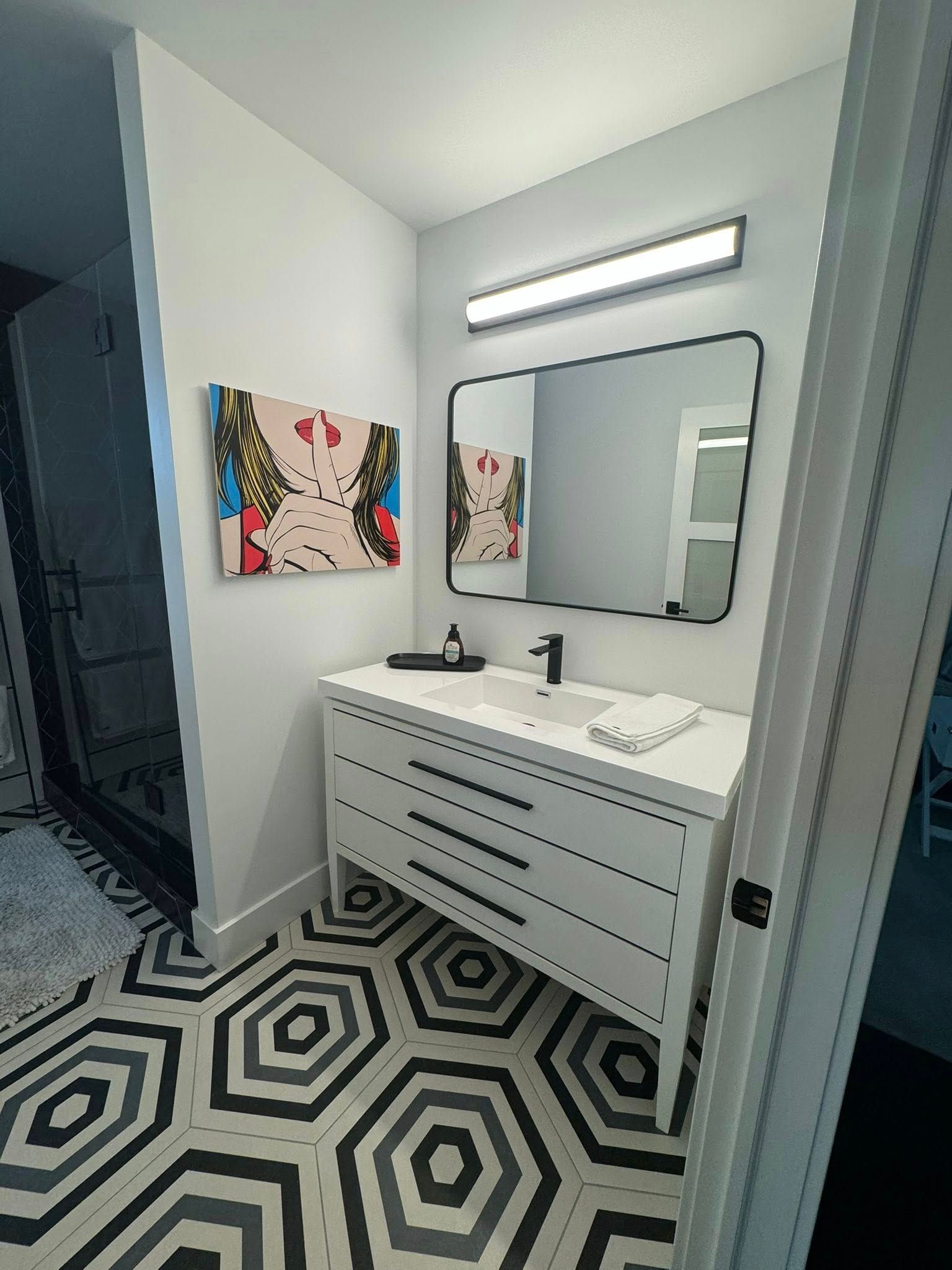 Bathroom with white vanity, black hexagon tile floor, and framed mirror.