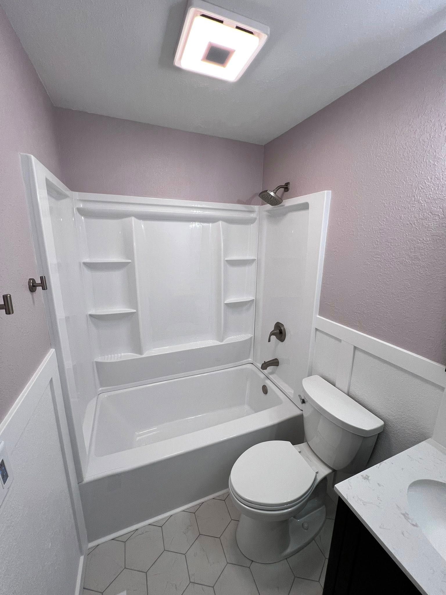 White bathroom with shower/tub combo, toilet, vanity, lavender walls, and patterned tile floor.