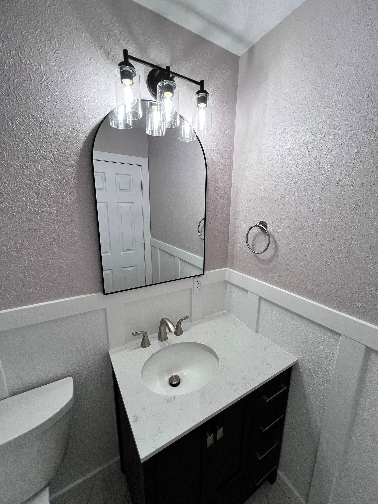 Small bathroom with a black vanity, arched mirror, and sparkly pink walls.