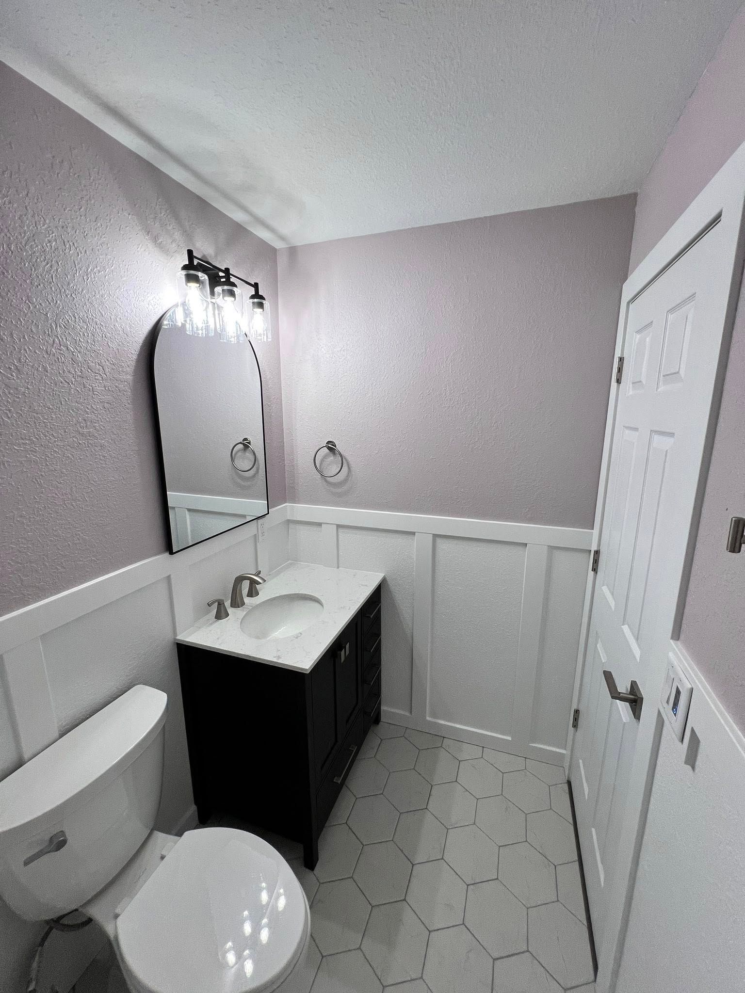 A small bathroom with white wainscoting and hexagon tile floor; black vanity and door; purple walls.
