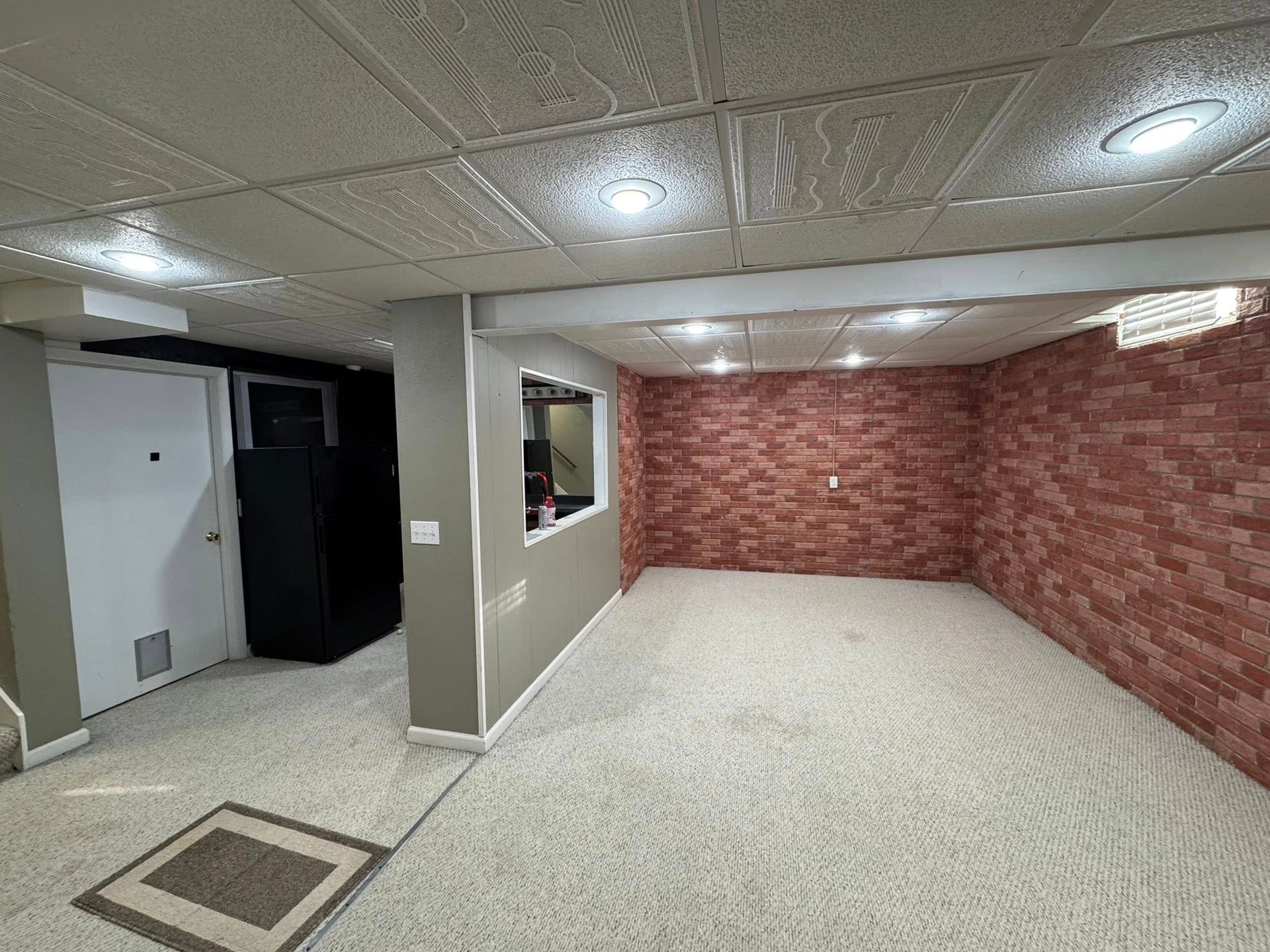 Basement room with white ceiling, brick wall, carpet, and a window.