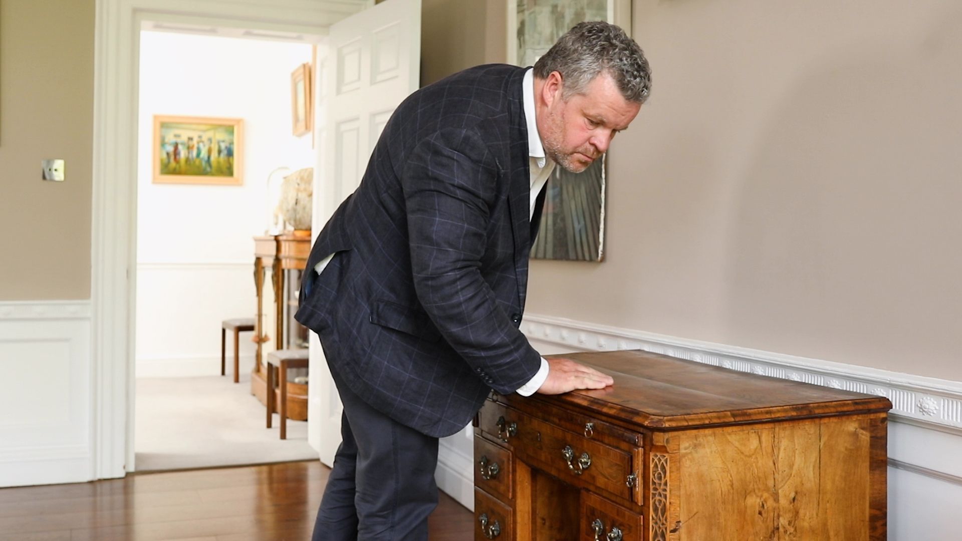 Quastel Associates | Valuation| Man bending over an ornate wooden chest in a bright hallway, examining or opening it.