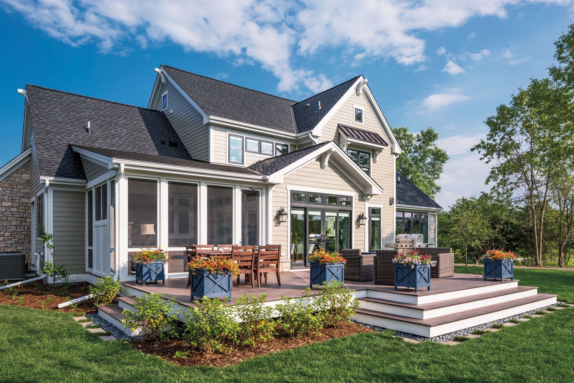 Backyard of a house with a deck, screened porch, and flower boxes on a sunny day.