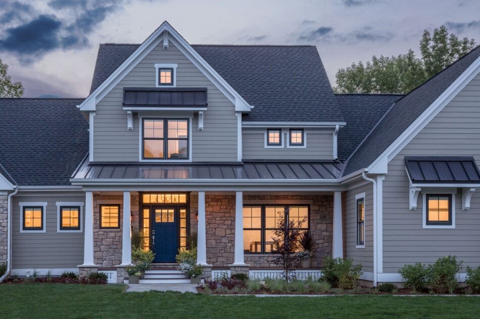 Gray and blue house with stone accents, porch, and dark roof at dusk.