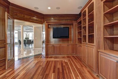 Wooden-paneled room with TV, built-in shelves, and open doors leading to a dining area with marble floor.