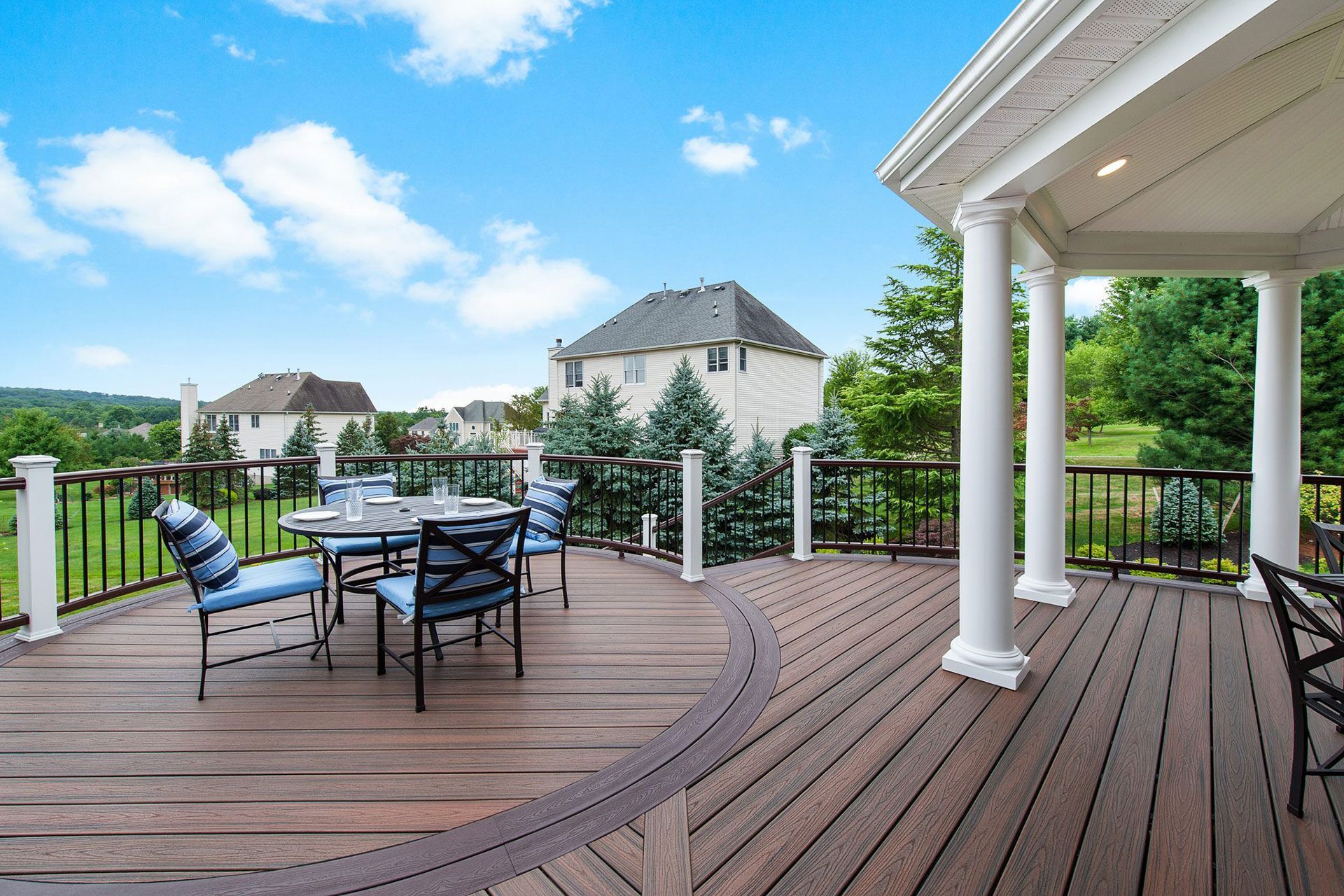 Deck with table and chairs overlooking a residential area on a sunny day.