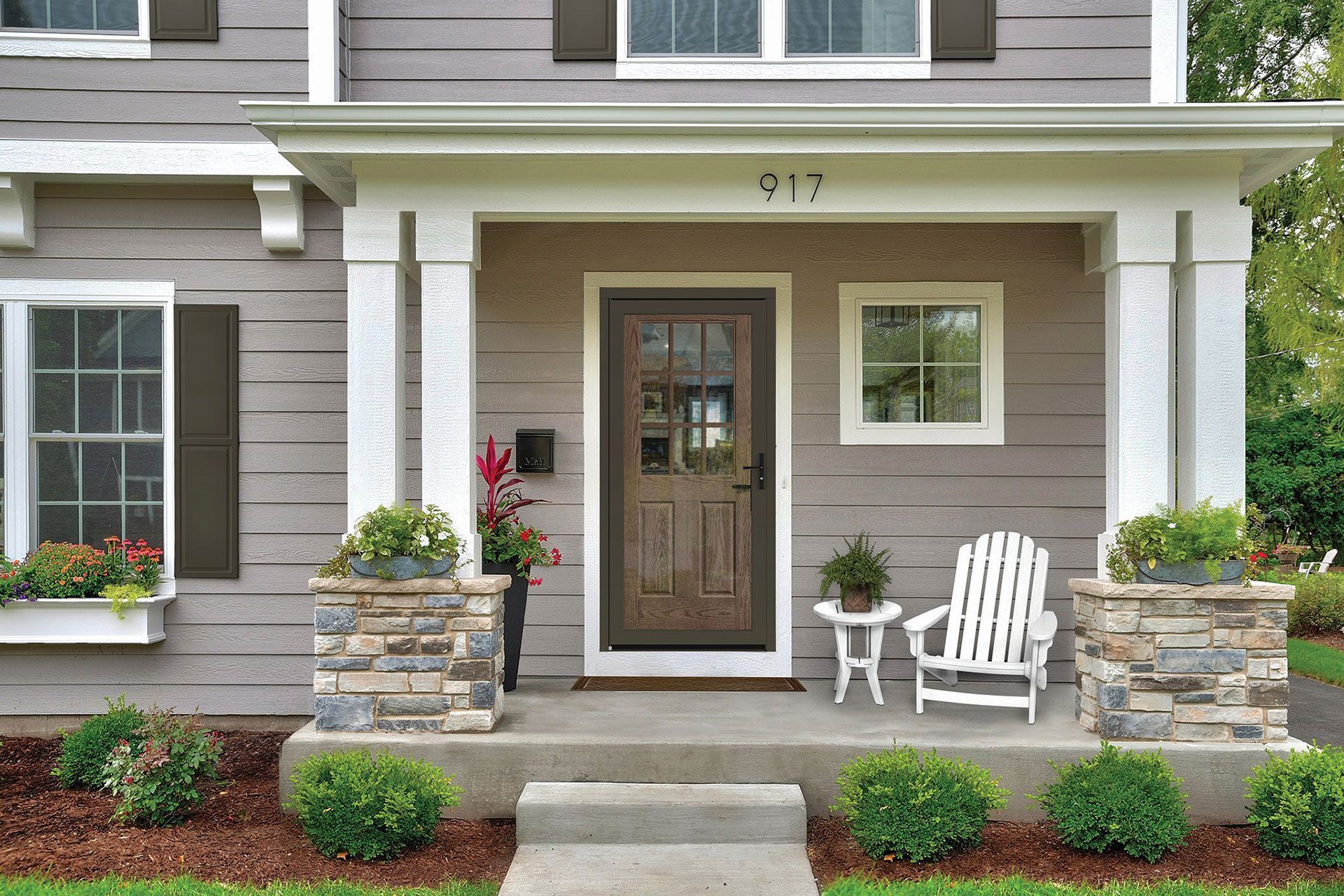 Front porch with a brown door, white chair, and potted plants in front of a grey house.