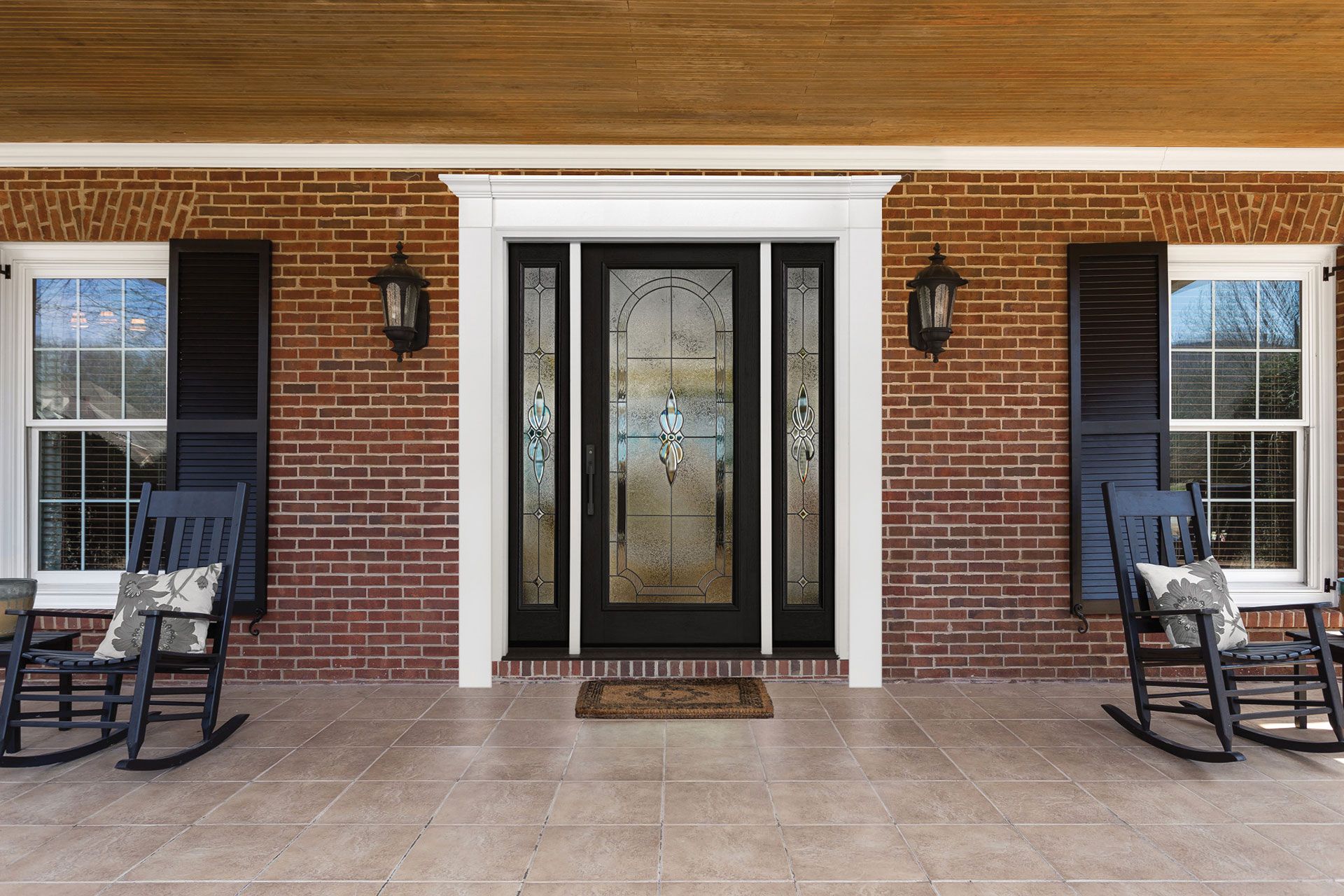 Front porch with black door, sidelights, brick wall, shutters, rocking chairs.