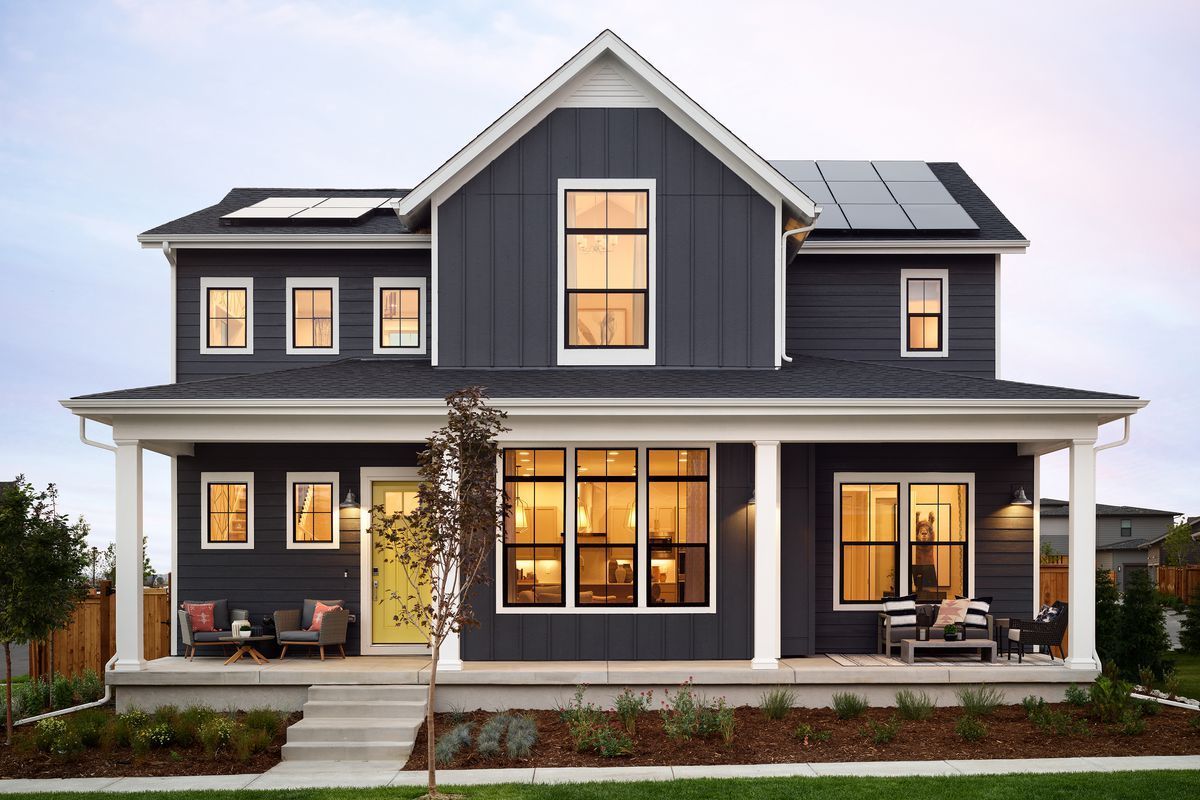 Dark blue two-story house with white trim, porch, and solar panels on the roof; evening setting.
