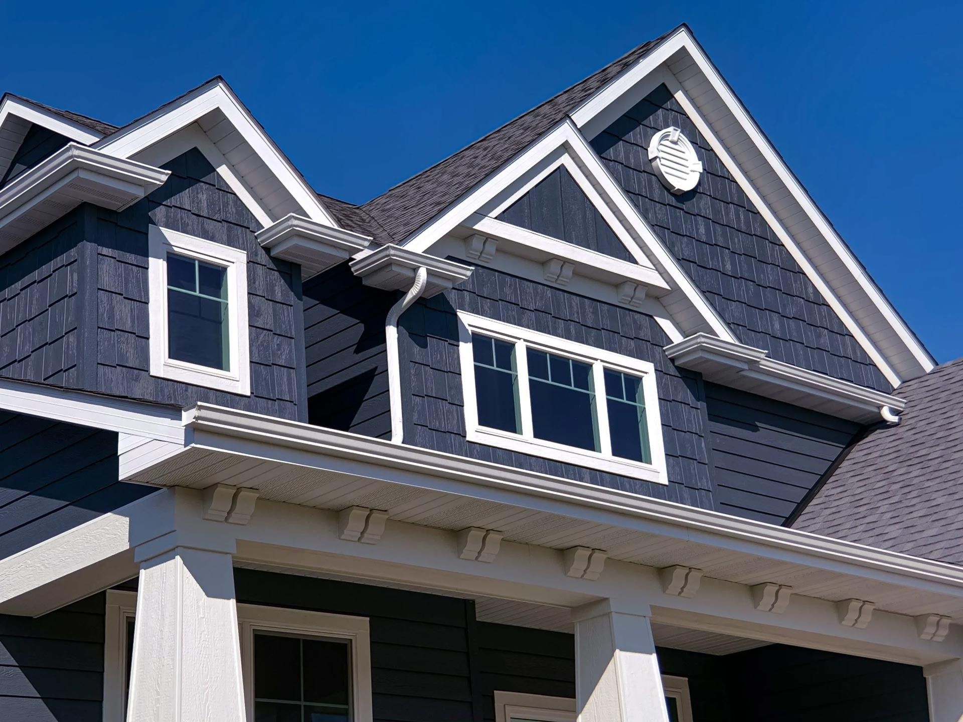 Blue-sided house with white trim, windows, and roof against a clear blue sky.