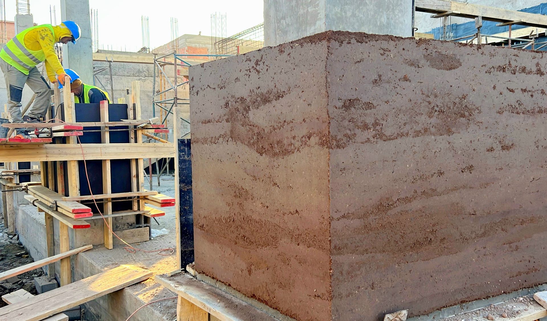 Des ouvriers du bâtiment construisent un mur en terre compressée ; ils utilisent des coffrages pour compacter le sol.