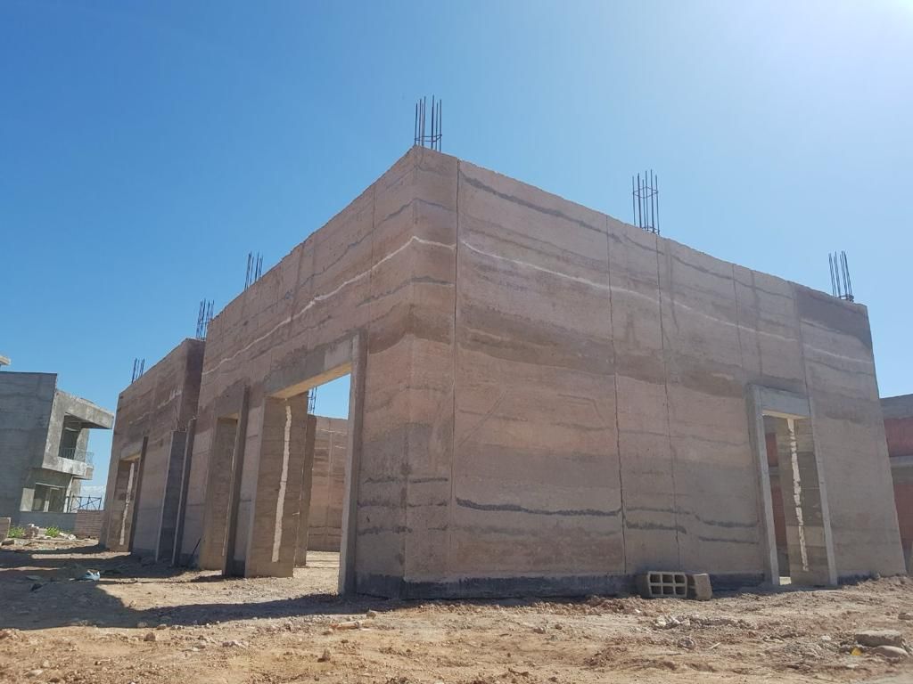 Construction en cours, murs en blocs de béton superposés sous un ciel bleu clair.