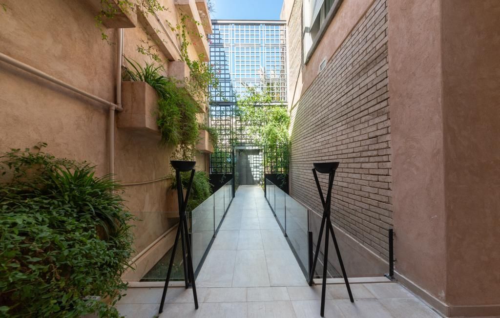 Passerelle à ciel ouvert dans une villa ;étroite entre les bâtiments avec des plantes et des garde-corps en verre.