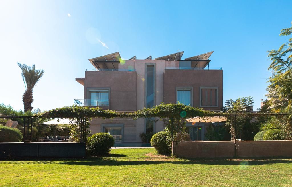 Maison moderne à deux étages avec panneaux solaires sur le toit, entourée d'un jardin bien strcuturé et arrosé.