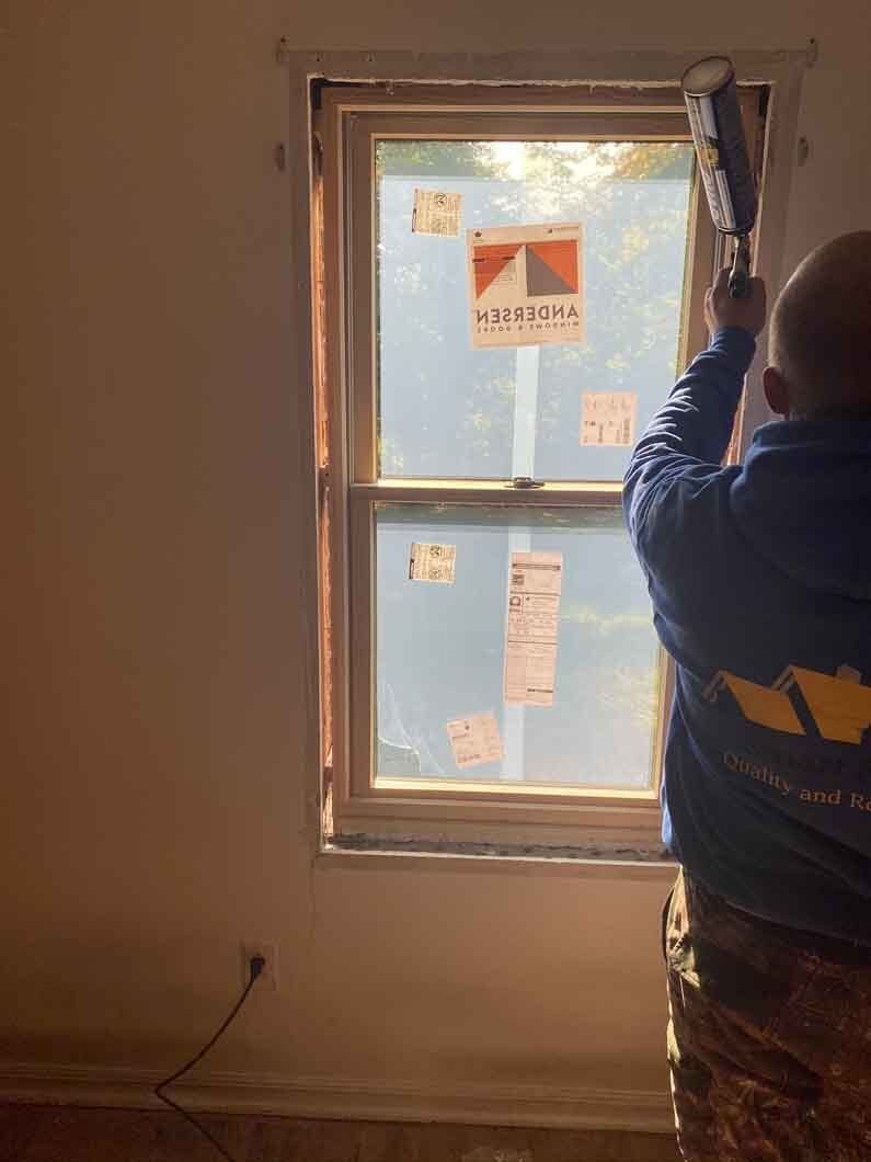 a man using a gun to paint a window.