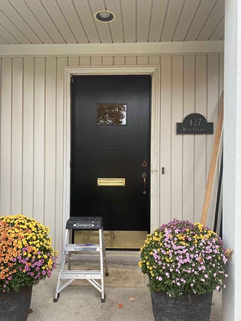 a black door with a step ladder and flowers.