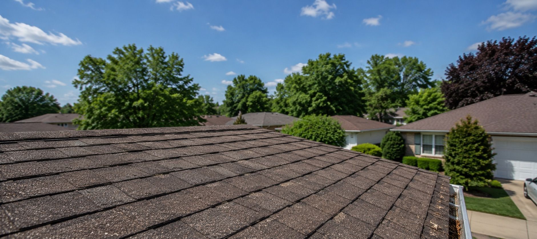 `Summer rooftop inspection in a suburban Michigan neighborhood with asphalt shingles, clear blue sky