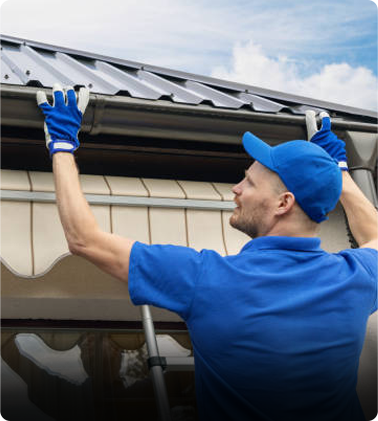 A man in blue clothing installing gutters on a building