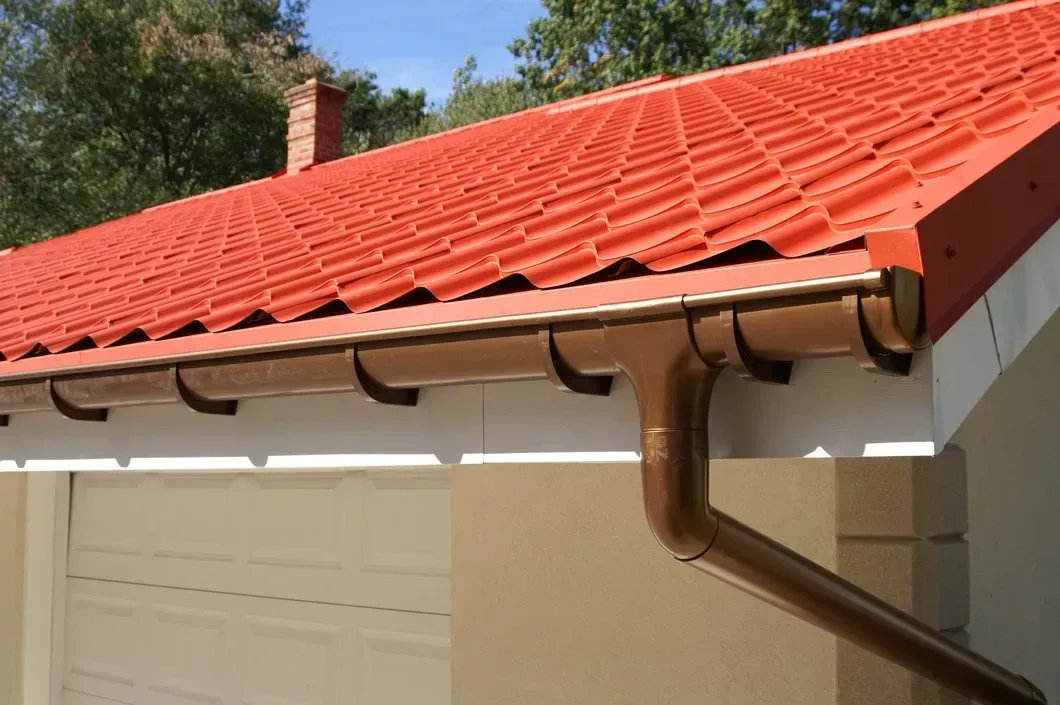 A close-up view of a residential building with a red tiled roof and a brown gutter, showcasing the architectural details