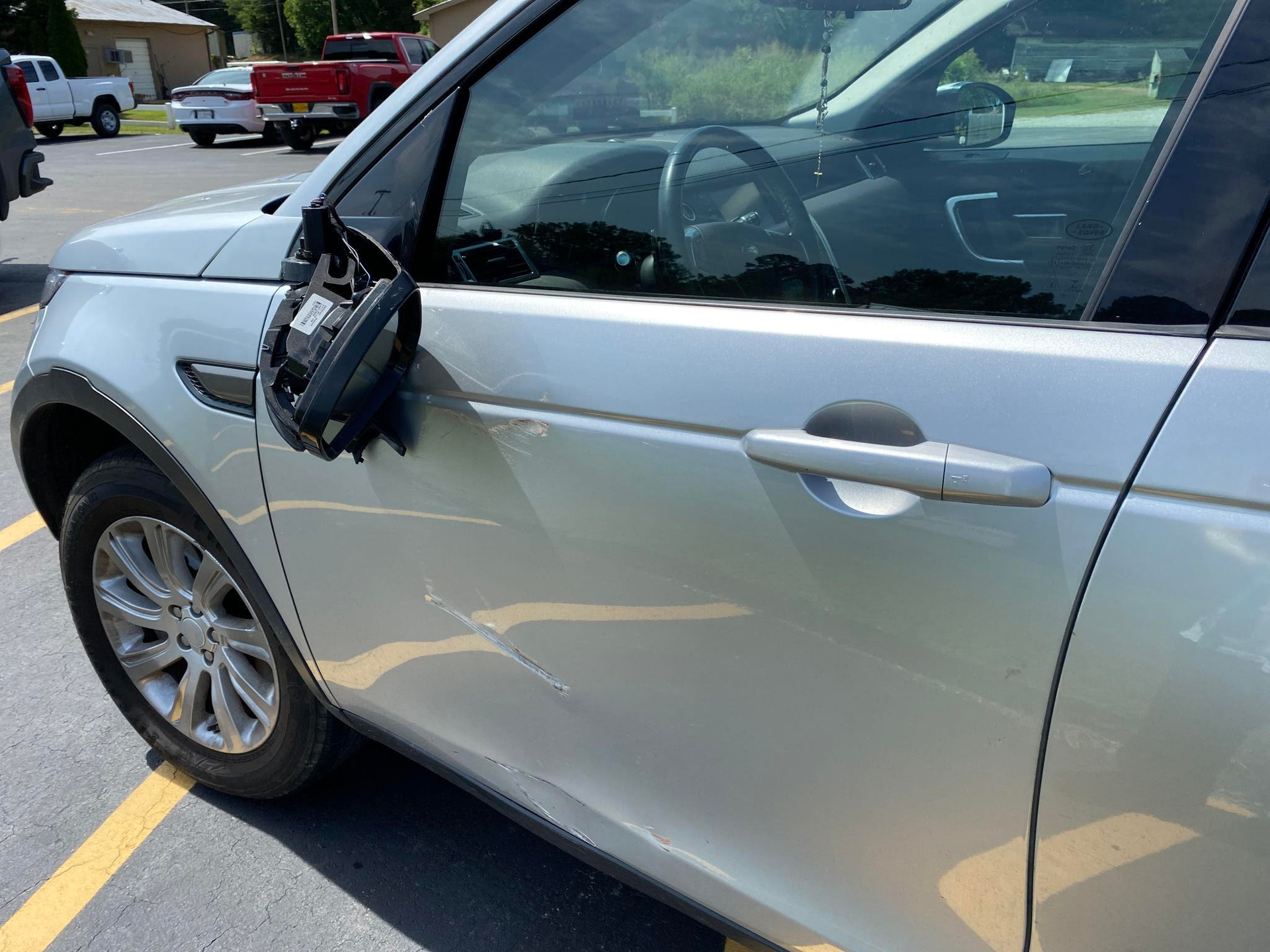A silver car with a broken side mirror is parked in a parking lot.  | Windham Bodyshop