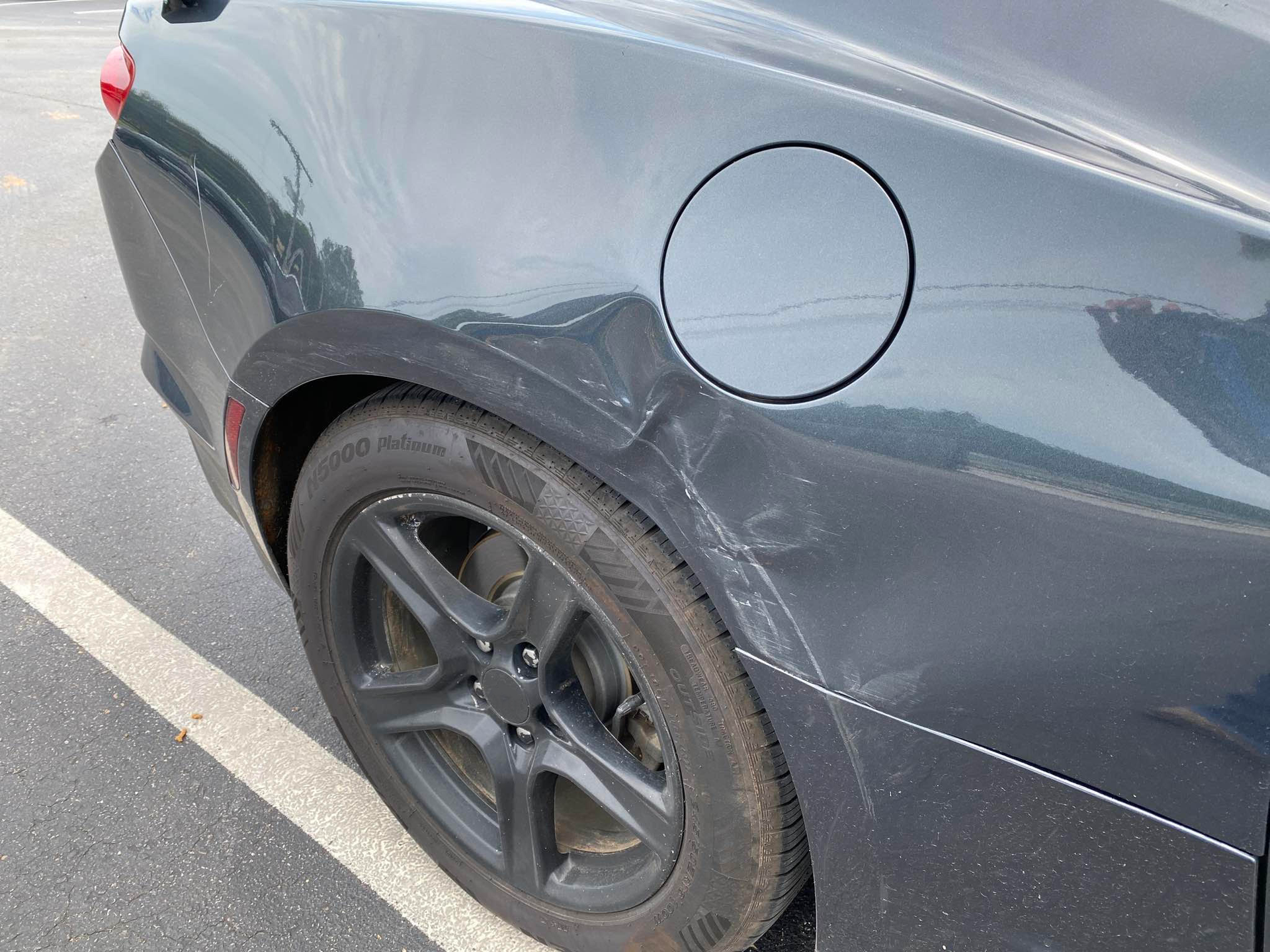 A black car with a damaged fender is parked in a parking lot.  | Windham Bodyshop
