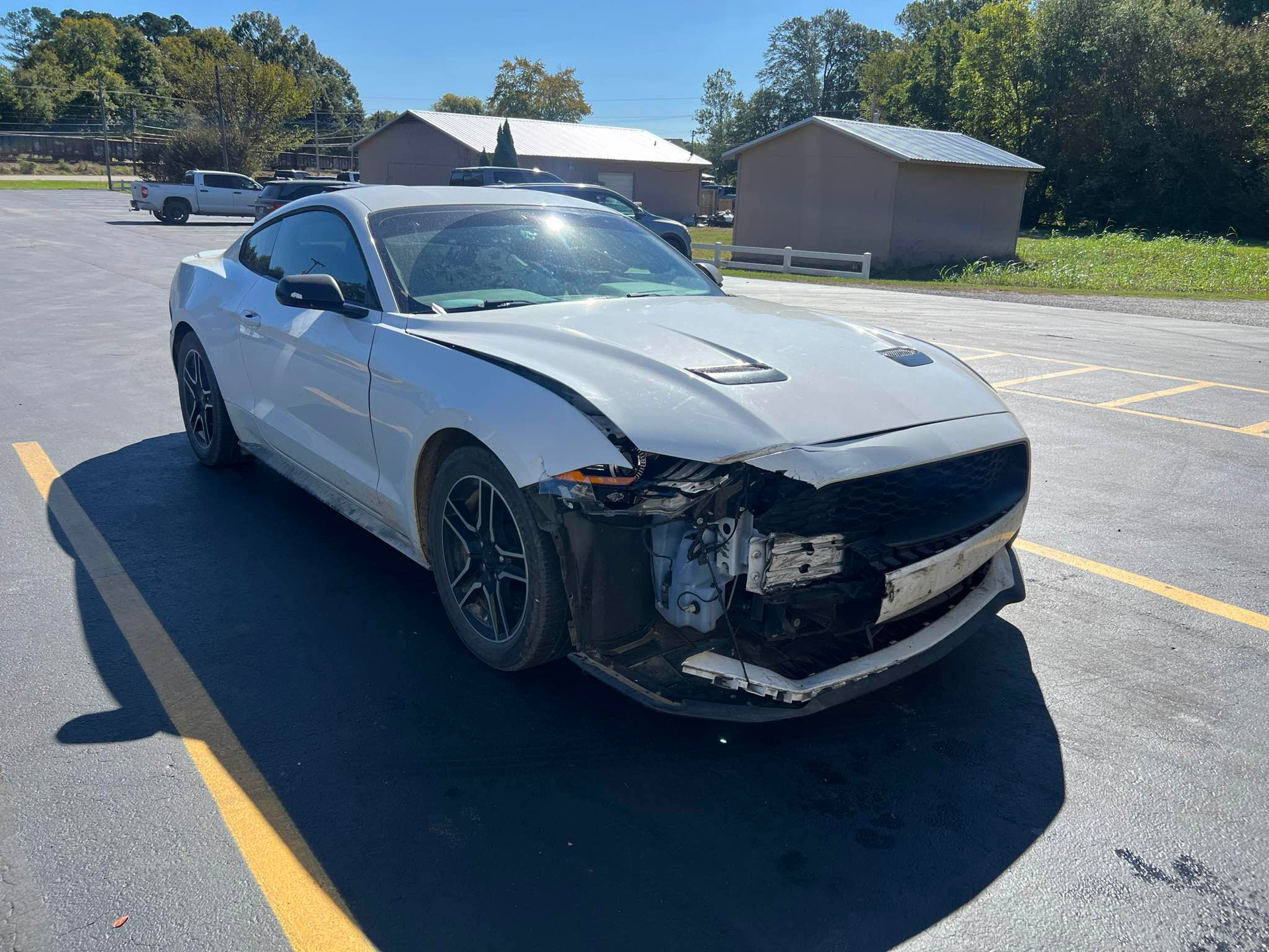 A white ford mustang with a damaged front end is parked in a parking lot.  | Windham Bodyshop