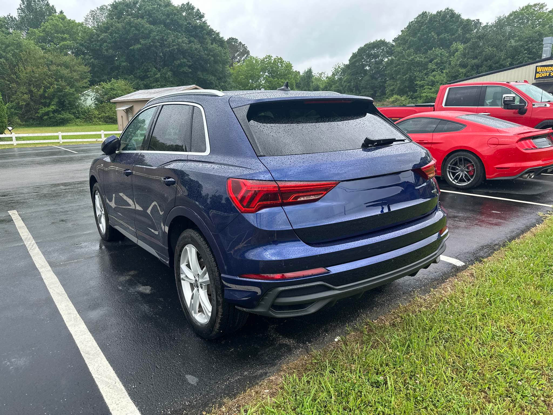 A blue car is parked in a parking lot next to a red truck.  | Windham Bodyshop