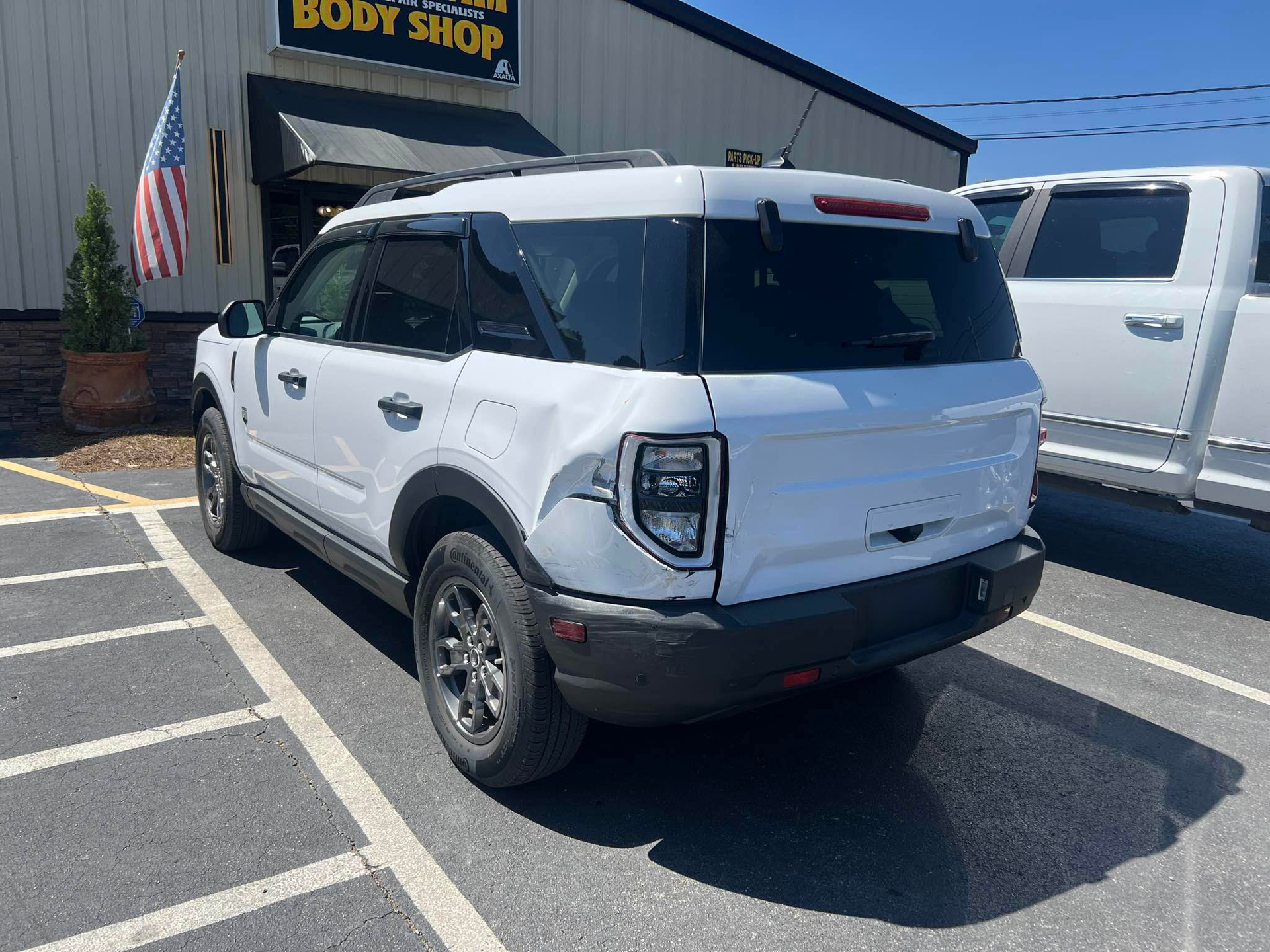 A white suv is parked in a parking lot in front of a body shop.  | Windham Bodyshop