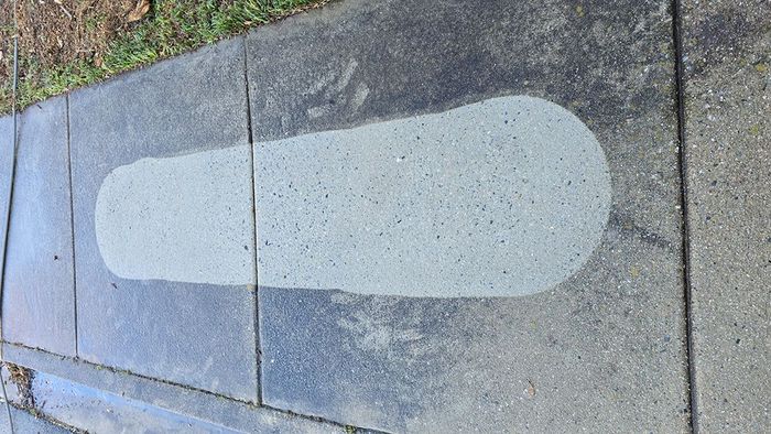 A skateboard is painted on a sidewalk next to a grassy area.