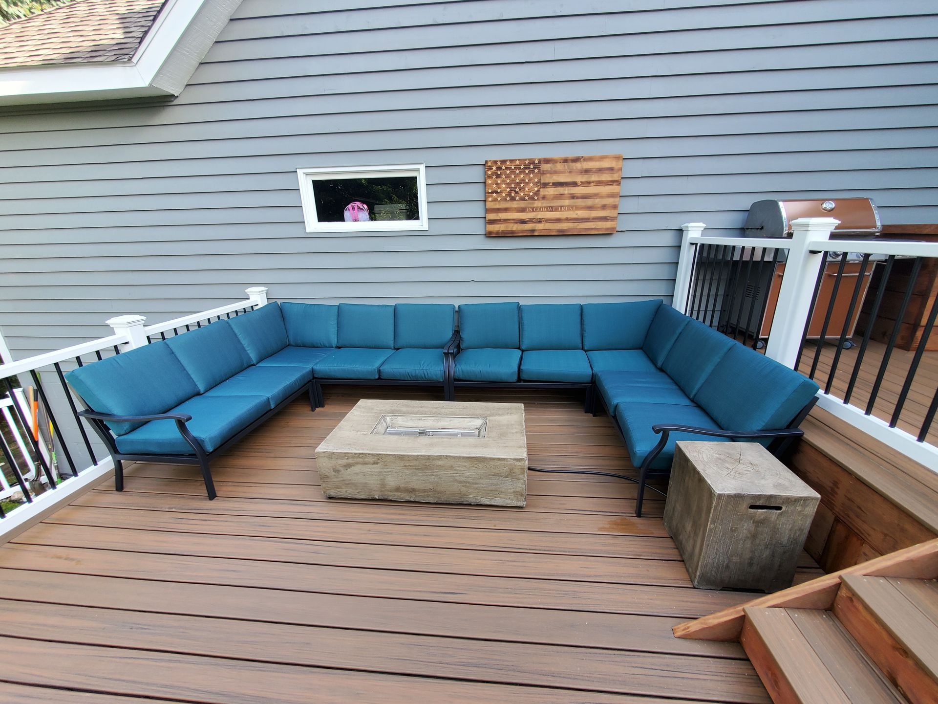 A large sectional couch is sitting on a wooden deck next to a fire pit.
